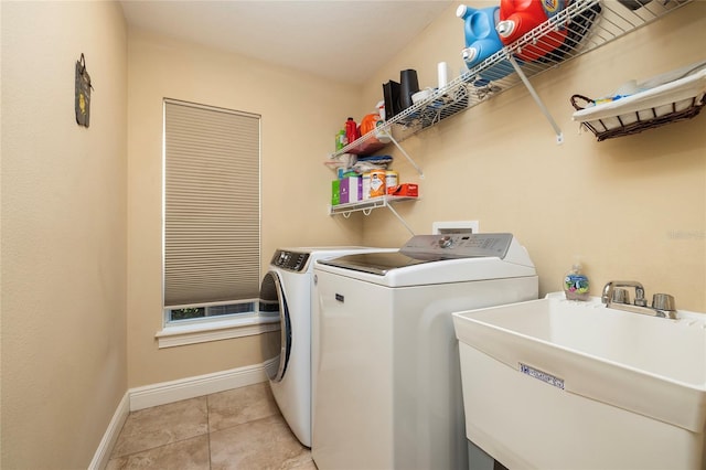 clothes washing area with washing machine and clothes dryer, baseboards, light tile patterned floors, laundry area, and a sink