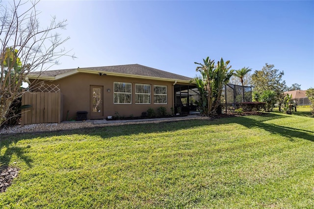 rear view of property featuring glass enclosure, fence, a lawn, and stucco siding