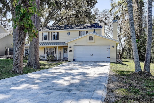 view of front of home featuring a front lawn, covered porch, a chimney, decorative driveway, and a garage