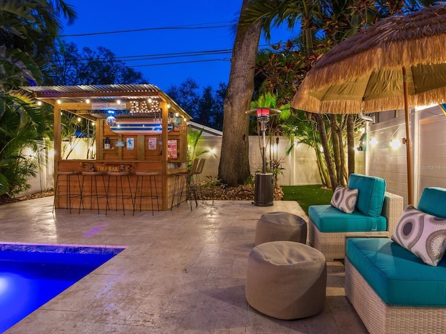 patio at twilight with a fenced backyard, outdoor dry bar, and an outdoor hangout area