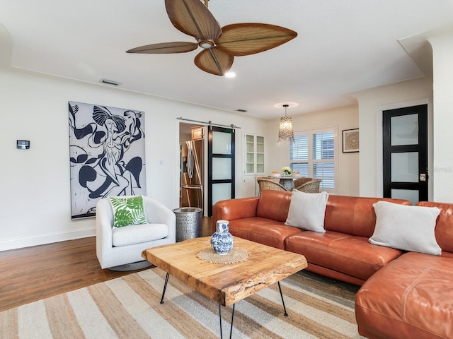 living area with visible vents, a ceiling fan, wood finished floors, a barn door, and baseboards