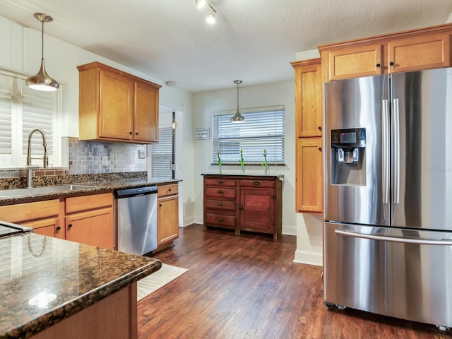 kitchen with tasteful backsplash, dark wood-style flooring, dark stone countertops, appliances with stainless steel finishes, and a sink