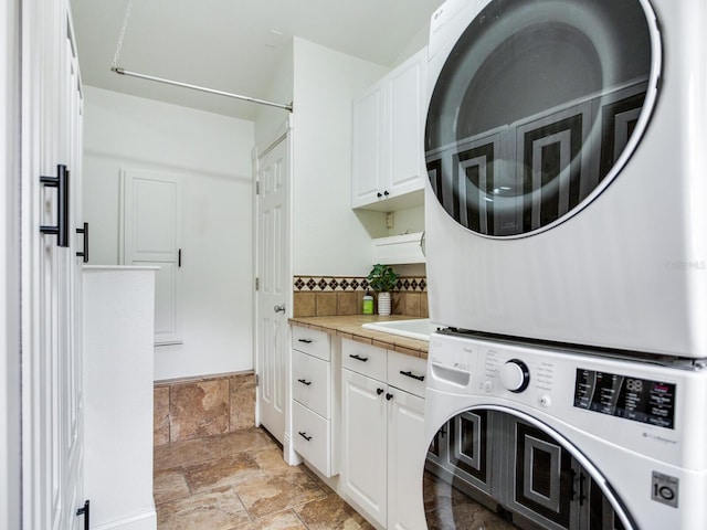 washroom with stacked washer / drying machine, cabinet space, and stone finish flooring