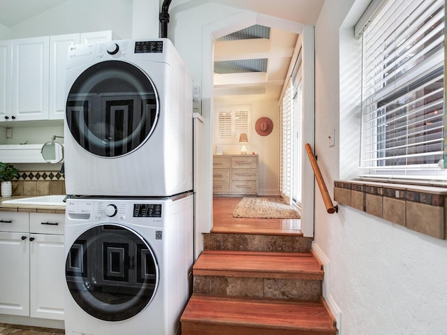 washroom with cabinet space, baseboards, and stacked washer and dryer