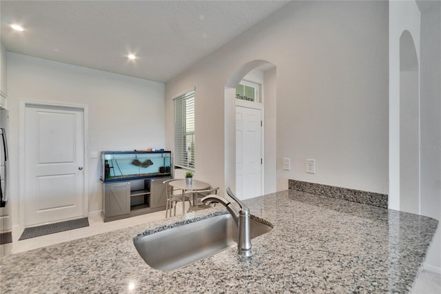 kitchen featuring a sink, stone counters, arched walkways, and recessed lighting