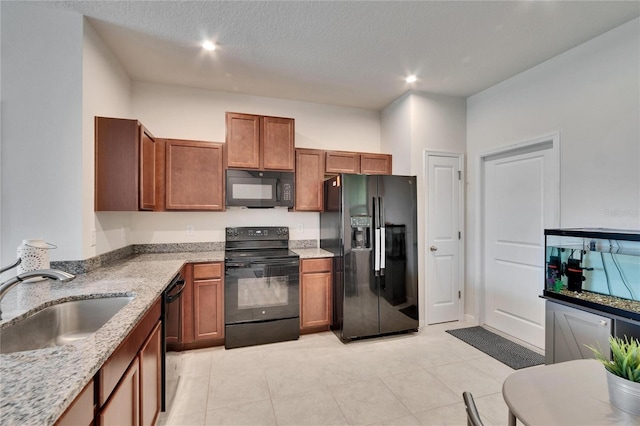 kitchen with light stone countertops, recessed lighting, brown cabinets, black appliances, and a sink