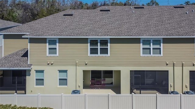 rear view of property featuring a patio area, fence, roof with shingles, and stucco siding