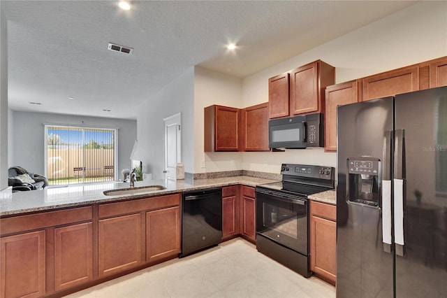 kitchen with light stone counters, visible vents, black appliances, and a sink