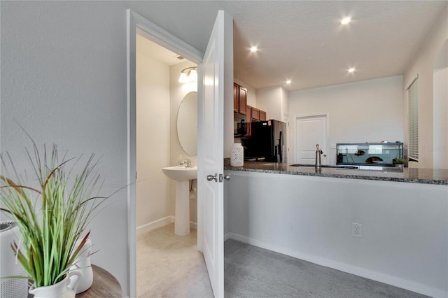 kitchen with recessed lighting, dark stone counters, baseboards, light colored carpet, and black refrigerator with ice dispenser