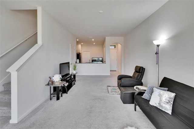 carpeted living room featuring stairway, baseboards, and arched walkways