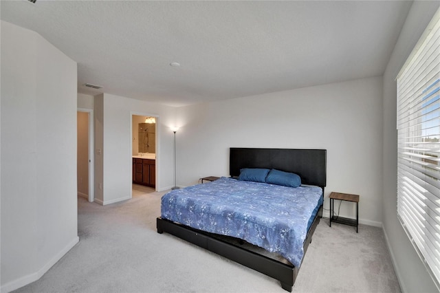 bedroom featuring visible vents, baseboards, ensuite bathroom, a textured ceiling, and light carpet