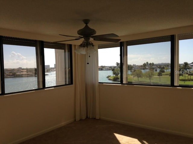 spare room with carpet flooring, a ceiling fan, baseboards, and a water view