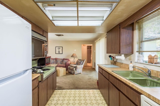 kitchen with open floor plan, light colored carpet, light countertops, white appliances, and a sink