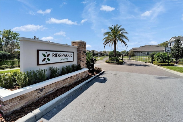 community sign featuring a gate, fence, and driveway