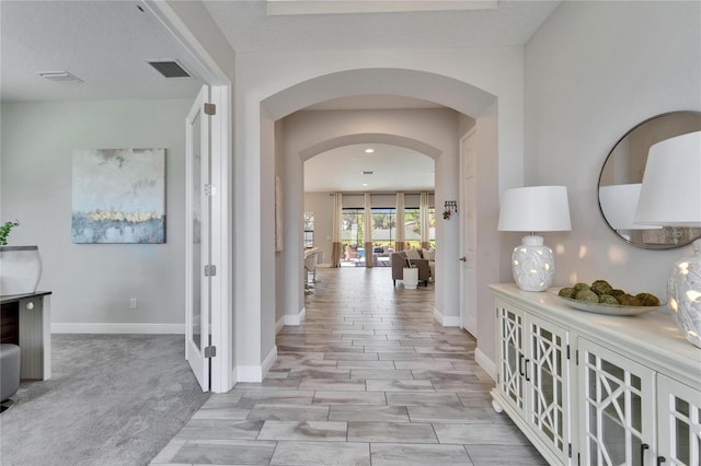 hallway featuring visible vents, arched walkways, and baseboards