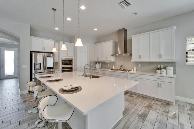 kitchen with visible vents, a sink, appliances with stainless steel finishes, wall chimney exhaust hood, and decorative backsplash