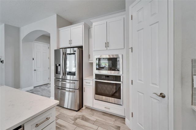 kitchen featuring light stone counters, a textured ceiling, white cabinetry, arched walkways, and appliances with stainless steel finishes