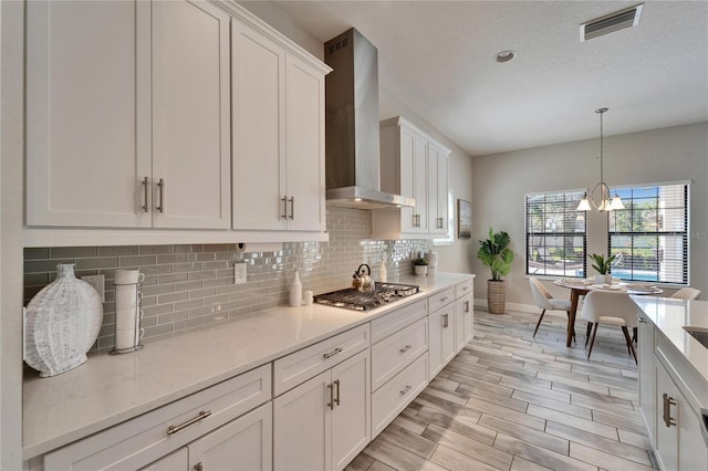 kitchen featuring white cabinetry, wall chimney range hood, backsplash, and stainless steel gas cooktop