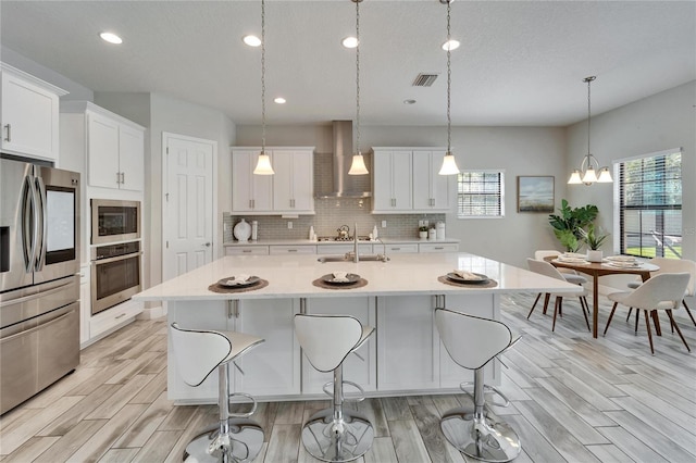 kitchen with visible vents, wall chimney range hood, wood tiled floor, light countertops, and appliances with stainless steel finishes