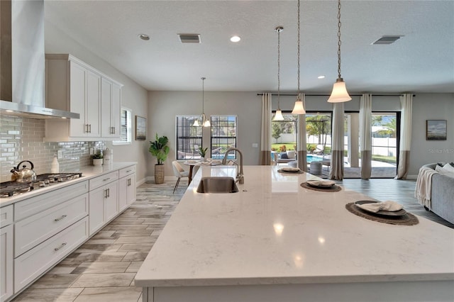 kitchen featuring visible vents, a sink, tasteful backsplash, wall chimney range hood, and stainless steel gas cooktop