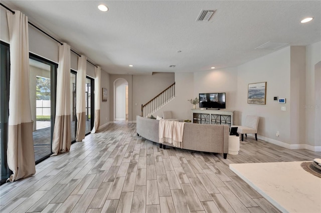 living area with light wood finished floors, visible vents, stairs, recessed lighting, and arched walkways