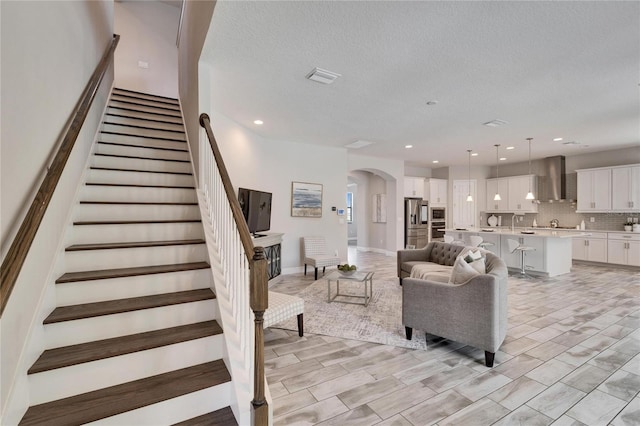 living area with visible vents, recessed lighting, arched walkways, stairs, and a textured ceiling