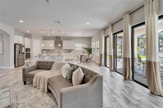 living room with recessed lighting, visible vents, light wood-style flooring, and a textured ceiling