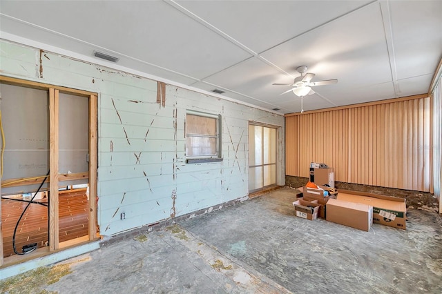 miscellaneous room featuring a ceiling fan, concrete block wall, visible vents, and unfinished concrete flooring