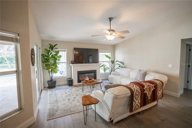 living area with baseboards, ceiling fan, lofted ceiling, wood finished floors, and a glass covered fireplace