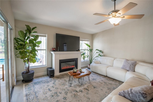 living room featuring a glass covered fireplace, a healthy amount of sunlight, baseboards, and a ceiling fan