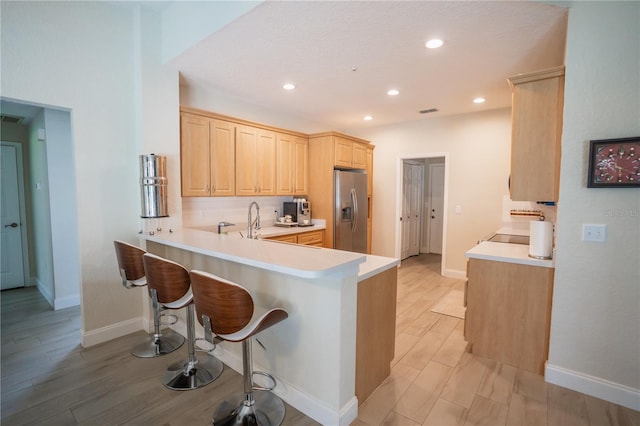 kitchen featuring wood tiled floor, light brown cabinetry, a breakfast bar area, a peninsula, and stainless steel refrigerator with ice dispenser