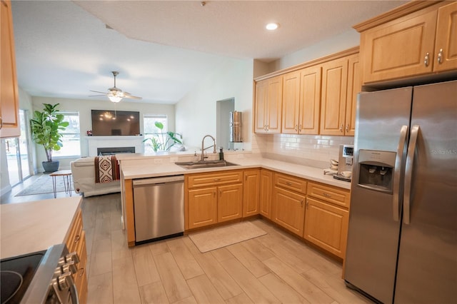 kitchen with open floor plan, light countertops, appliances with stainless steel finishes, a peninsula, and a sink