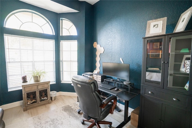 home office featuring a textured wall, baseboards, and wood finished floors