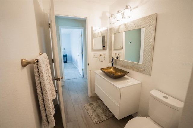 half bathroom with toilet, vanity, and wood finished floors