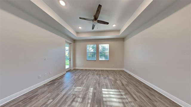 spare room featuring baseboards, recessed lighting, wood finished floors, a raised ceiling, and a ceiling fan