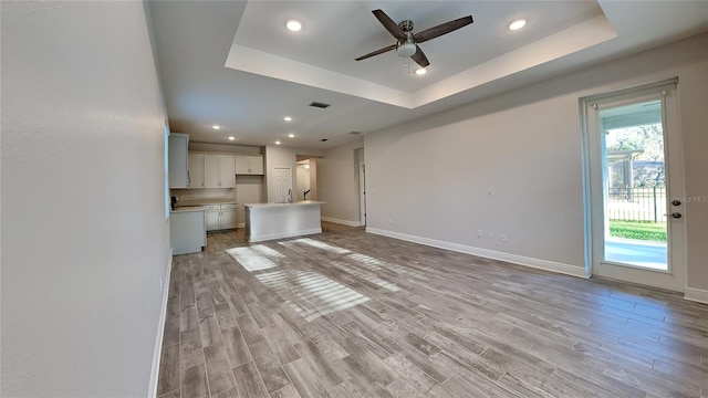 unfurnished living room with a raised ceiling, baseboards, light wood finished floors, and ceiling fan