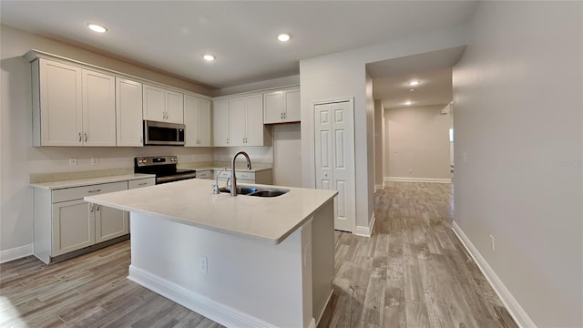 kitchen with light wood-type flooring, a center island with sink, a sink, stainless steel appliances, and light countertops