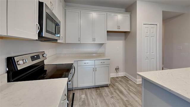 kitchen with stainless steel appliances, white cabinets, light wood finished floors, baseboards, and light stone countertops