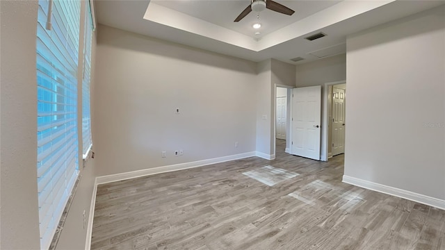 unfurnished bedroom with wood finished floors, baseboards, visible vents, ceiling fan, and a raised ceiling