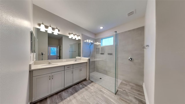 full bath featuring wood finished floors, visible vents, double vanity, a sink, and a walk in shower