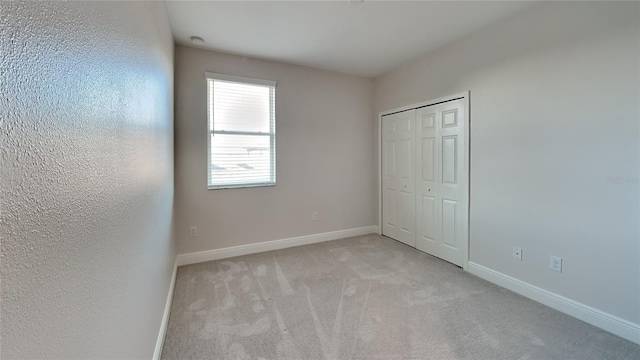 unfurnished bedroom with baseboards, light carpet, and a closet