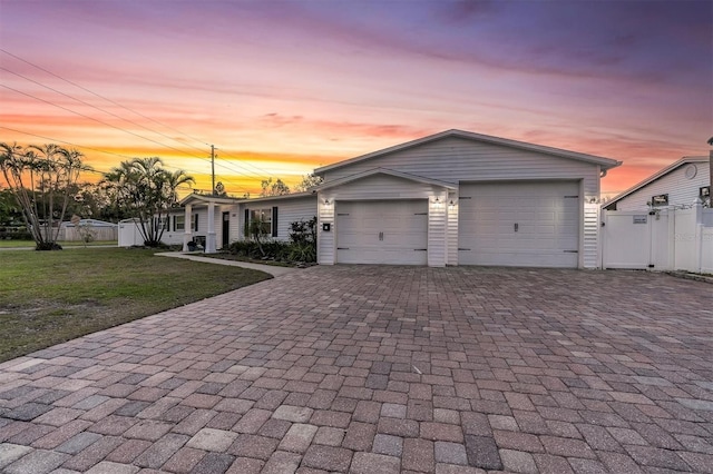 view of front of property with a lawn, an attached garage, a gate, fence, and decorative driveway