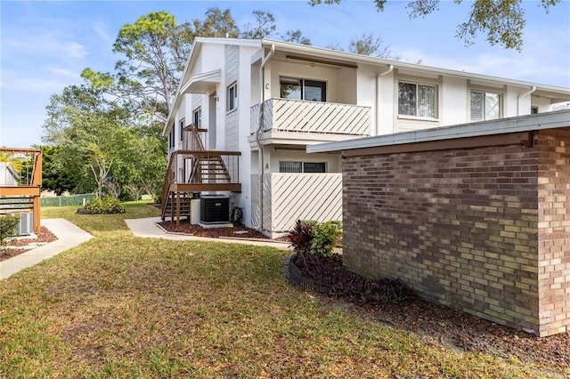 view of property exterior featuring central air condition unit, brick siding, stairs, a yard, and stucco siding