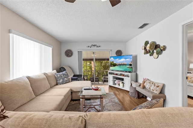 living room with a ceiling fan, a textured ceiling, visible vents, and wood finished floors