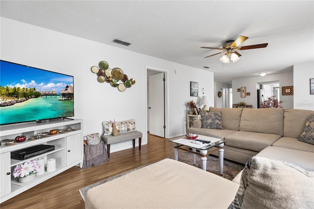 living room featuring a ceiling fan, a textured ceiling, visible vents, and wood finished floors