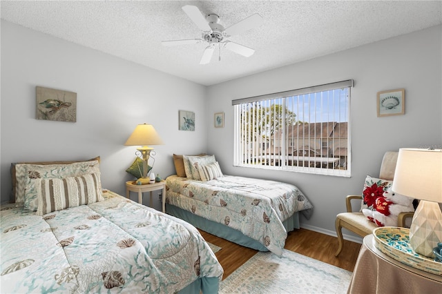 bedroom featuring ceiling fan, a textured ceiling, baseboards, and wood finished floors