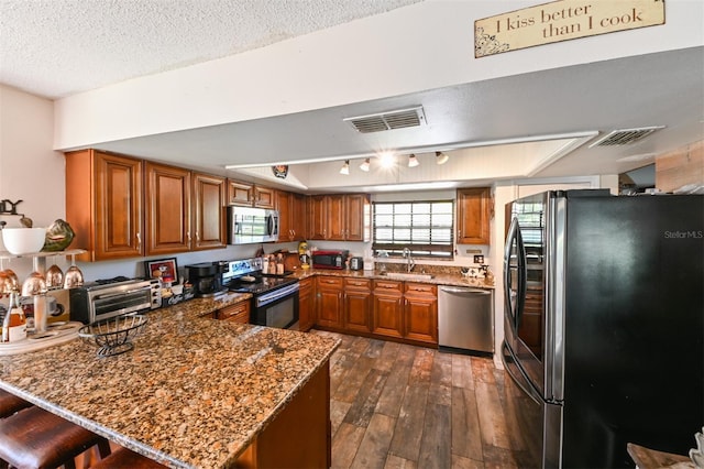 kitchen featuring a peninsula, visible vents, appliances with stainless steel finishes, and brown cabinetry