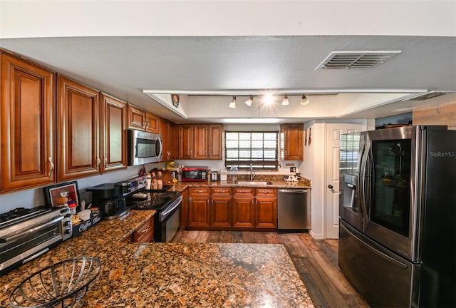 kitchen with dark wood-style flooring, a sink, visible vents, appliances with stainless steel finishes, and brown cabinetry