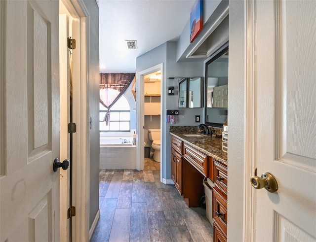 bathroom featuring visible vents, toilet, wood finished floors, a garden tub, and vanity