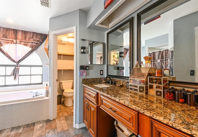 bathroom with visible vents, a garden tub, vanity, and toilet